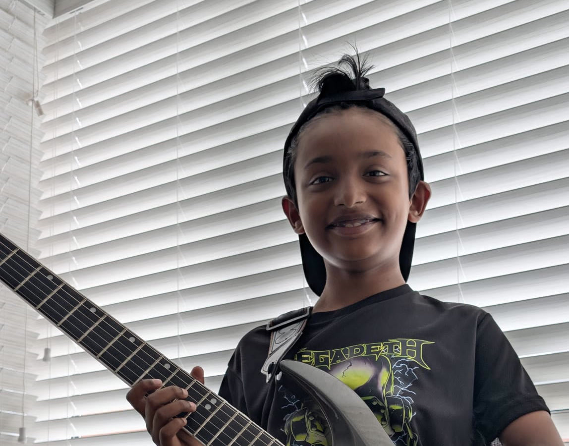Adrian Abraham smiling with his electric guitar at home