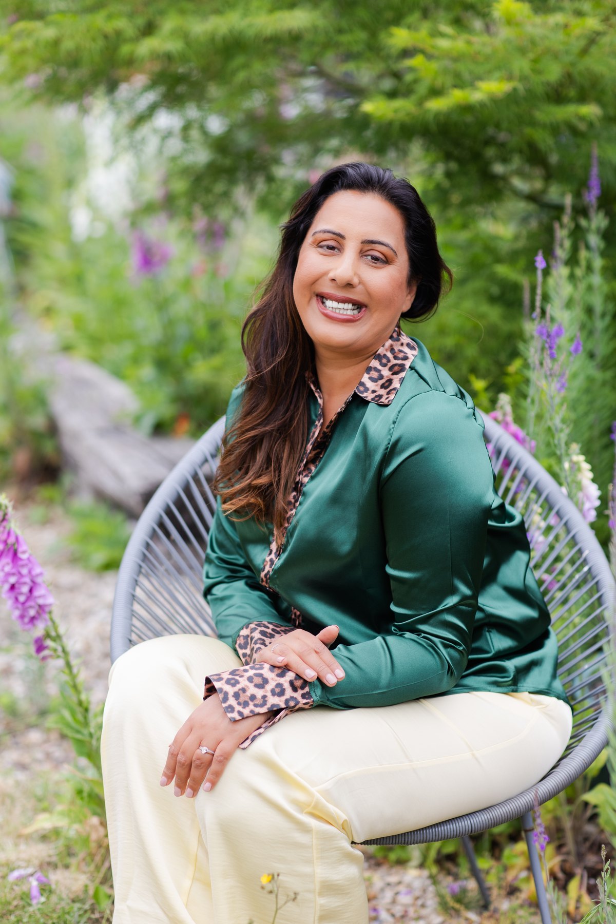 Nikita Thakrar laughing, seated in a garden, wearing a green blouse with leopard-print trim